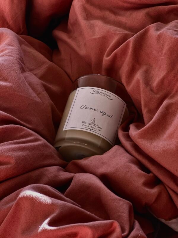 Gros plan sur le design élégant et le contenant en verre de la bougie de luxe 'Premier Regard', avec un style français minimaliste. Close-up of the elegant design and glass container of the 'Premier Regard' luxury candle, featuring a minimalist French style. flamme dleixir, flamme elixir, flame elixir, flamme delixir, elixir flame, elixir flamme, bougie de luxe, bougie luxe